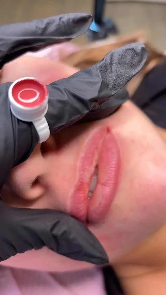 Gloved hands performing lip blush cosmetic tattoo procedure on a client