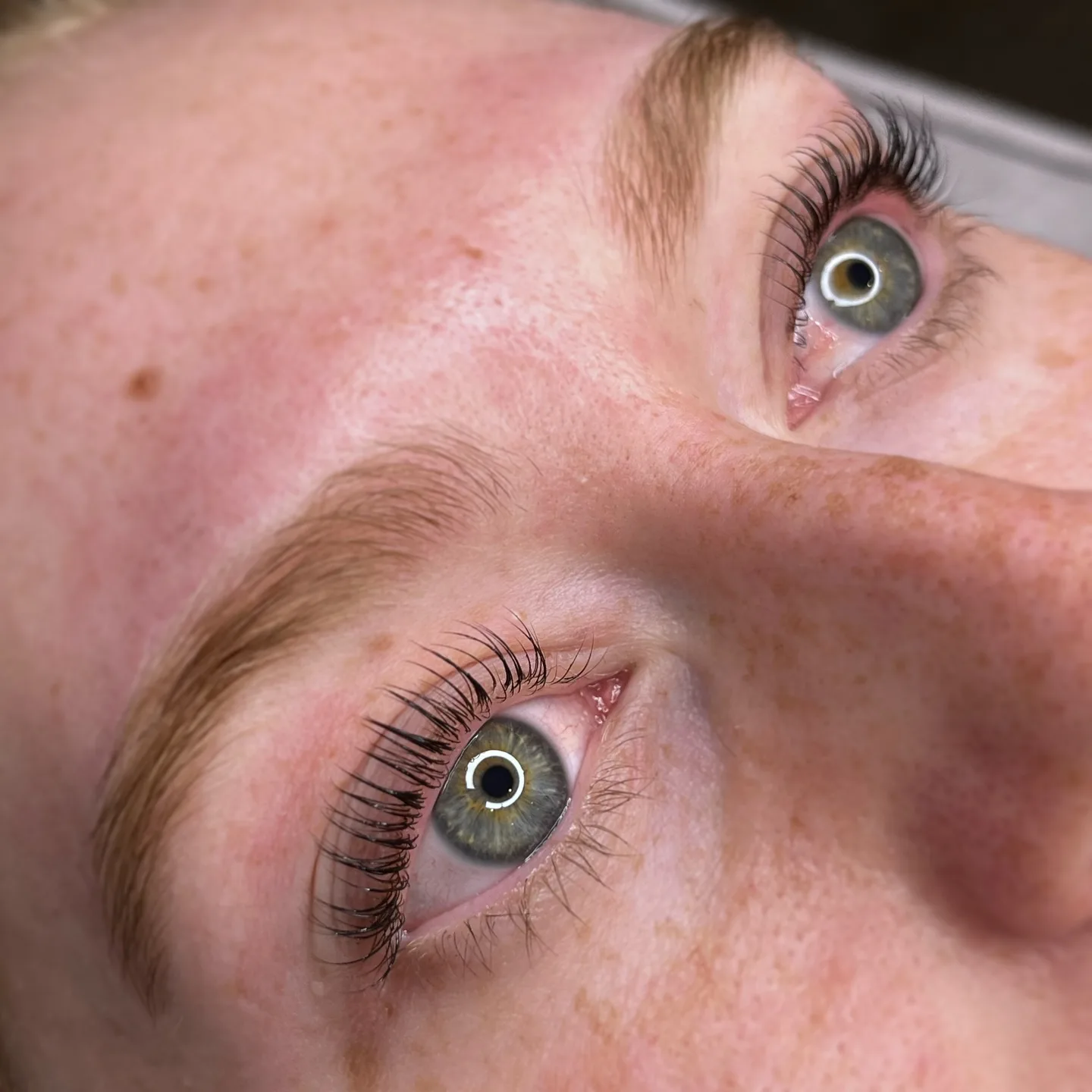 Korean lash lift result — lifted and defined natural lashes on a client with freckled skin, both eyes shown