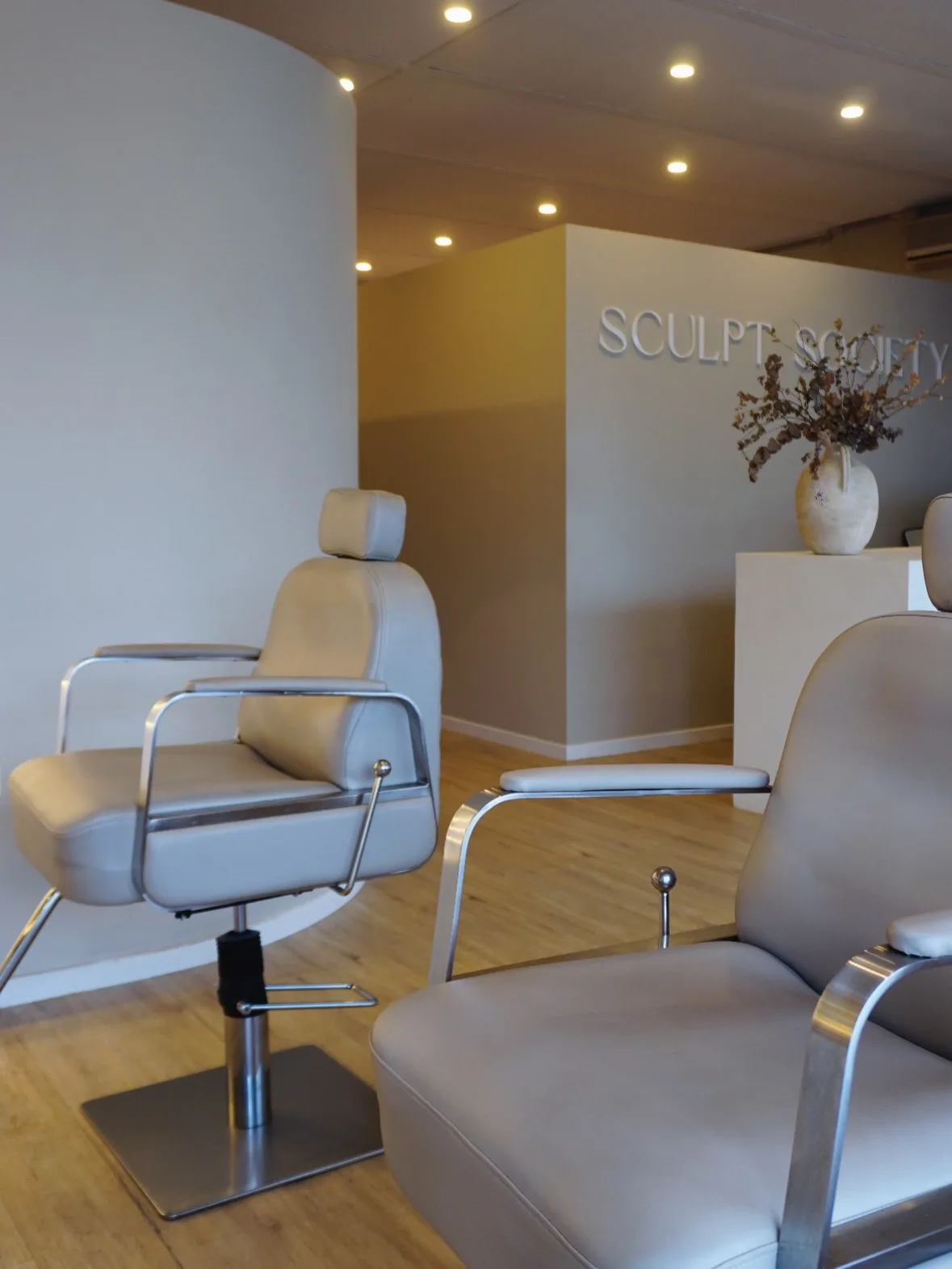Treatment room — twin cream chairs, oak floor, Sculpt Society wall signage
